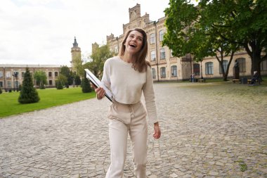 Şehirde dışarıda vakit geçirirken elinde evrak ve defter tutan neşeli gülen kadın.