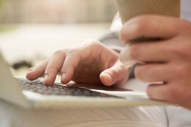 Elinde bir fincan kahveyle modern taşınabilir defter üzerinde çalışan bir adama yaklaş.