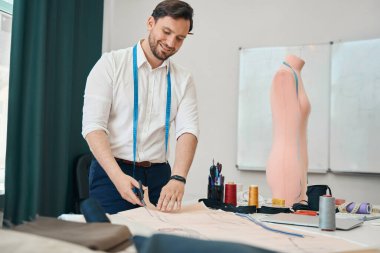 Bantlı neşeli genç terzi atölyedeki dikiş tasarımcıları için eskizler hazırlıyor.