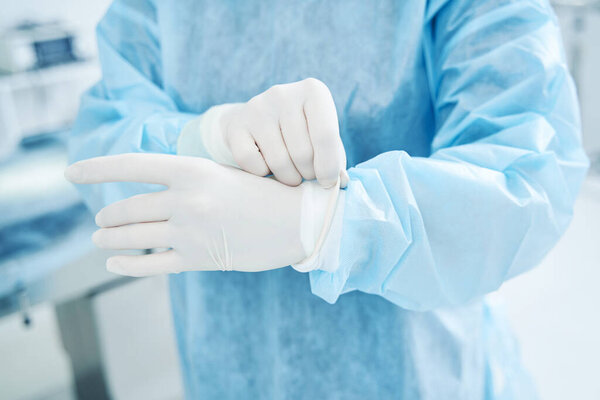Medical worker in a surgical gown putting latex gloves on the hands
