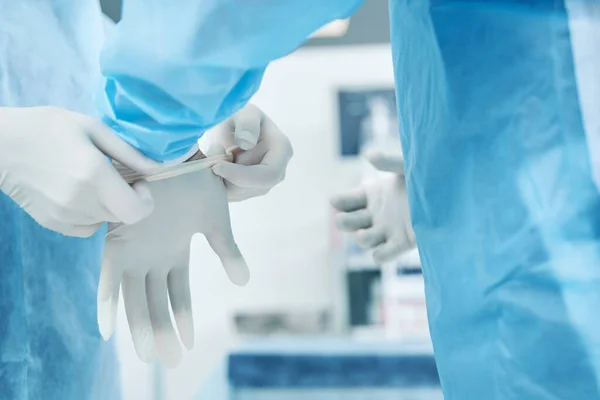 Close up of a doctor in a surgical gown putting a hand into a sterile latex glove