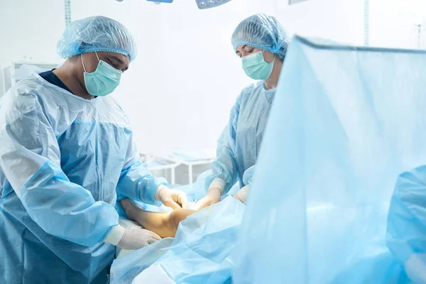 Concentrated doctors in medical clothes standing near the leg of their patient and curing varicose veins