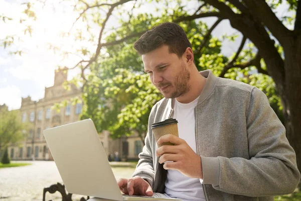テイクアウトドリンクのカップを持っている髭の男性と屋外での時間を過ごしながらノートブックで作業 — ストック写真