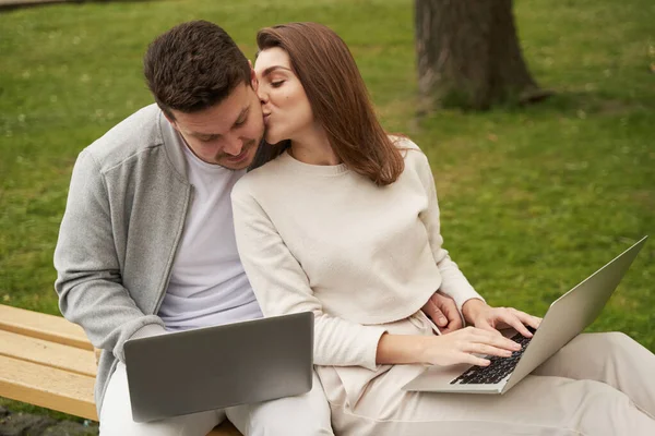 Mulher Apaixonada Sentada Banco Beijando Bochecha Homem Enquanto Trabalhava Notebook — Fotografia de Stock