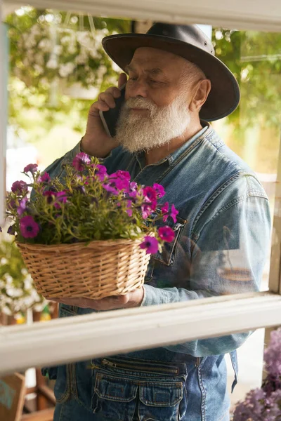 카우보이 모자를 쾌활하게 나이든 남자가 꽃바구니를 휴대폰으로 말하고 — 스톡 사진