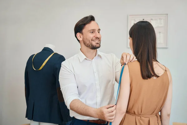 Uśmiechnięty Projektant Mody Jest Przy Użyciu Taśmy Ramieniu Kobiety Podczas — Zdjęcie stockowe