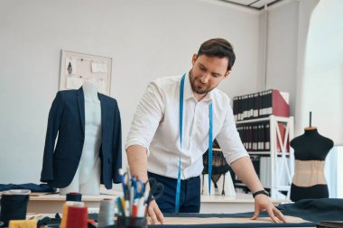 Sakin moda tasarımcısı, önündeki masada dikiş malzemeleri dururken kıyafet yapmak için hazırlık yapıyor.