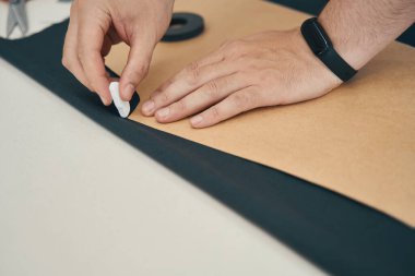 İnsan eli tebeşiri kağıt şablonunu takip etmek amacıyla tutarken diğer el de masayı kumaşa bastırıyor.