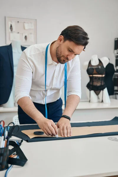 Focused fashion designer stands in the sewing room while hand outlines silhouette of future outfit