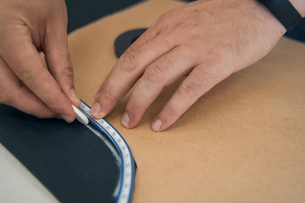 Hand by man presses a paper template against the fabric while the second hand traces a line along the contour