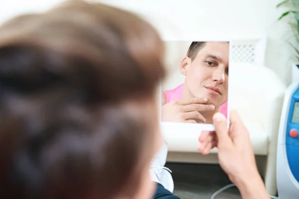 Mladý Muž Dívá Zrcadla Ruce Pro Sledování Obličeje Návštěvě Kosmetické — Stock fotografie