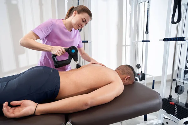 Smiling woman doctor massaging male back with physiotherapy vibration massage device
