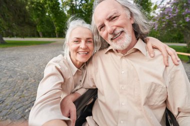 Cheerful blonde woman embracing her husband while being in park together