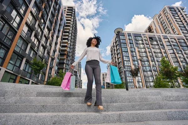 Happy multiracial woman walking down stairs with shopping bags