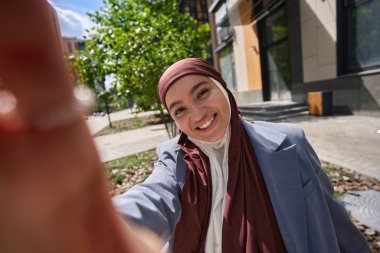 tesettürlü gülümseyen Arap kadın cep telefonundan selfie çekiyor.