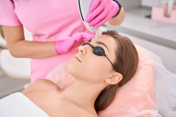 Dissatisfied woman spends time in beauty parlor while beautician works with device on her face