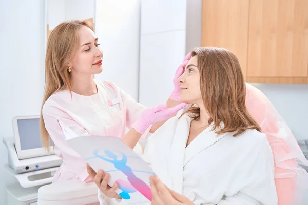 Relaxed Woman Sitting Information Booklet Medical Chair While Beautician Nearby — Stockfoto
