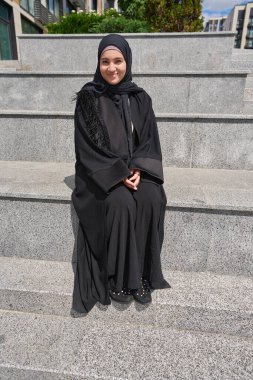 Korkulukta oturan tesettürlü güzel Arap kadın.