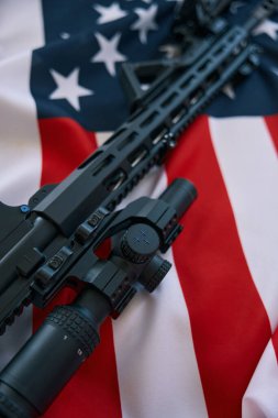 Sniper rifle with telescoping scope resting on flag of the USA
