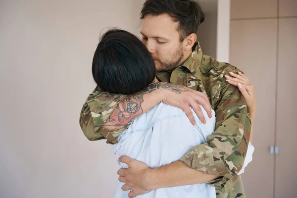 Male in military uniform hugging his romantic partner before going to war