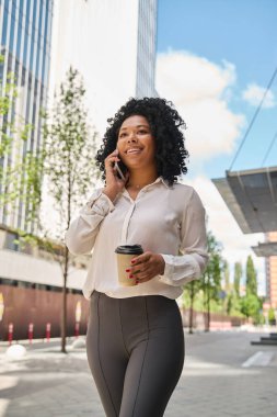 Ofisteki kadın kıyafetleri neşe içinde metropolün sokaklarında yürüyor. Yüksek binalar ve genç ağaçlar arasında.