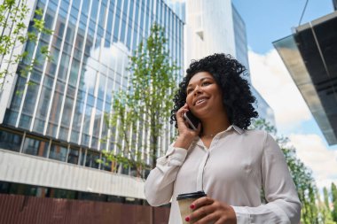 Metropolis sokaklarında neşeli bir yaz sabahı, ellerinde içki olan genç kadınlar telefonda gülümsüyor.