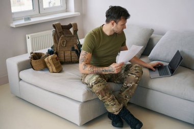 Ukrainian army serviceman using laptop from online communication while dealing with documentation work from home