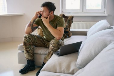 Kafkas ordusu mensubu evde telefonuna cevap bekliyor ve kanepede dizüstü bilgisayarın önünde Chin 'e dokunuyor.