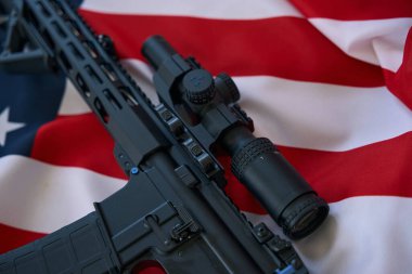 Black automatic rifle with optical scope laying on American flag