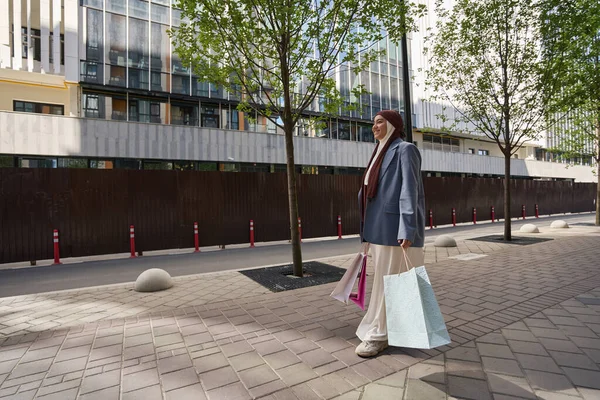 Smiling woman walking down a sunny street and carrying shopping bags