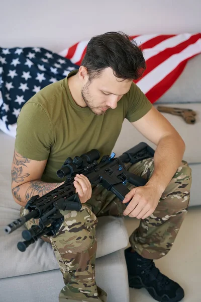 Caucasian Male Combatant Inspecting Checking His Gun While Sitting Sofa — Stockfoto