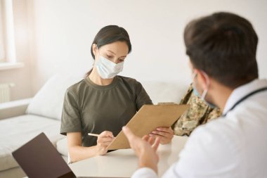 Medical workers at their desk confer and study the medical history of a military patient in a bright ward
