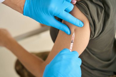 Nurse in protective gloves makes an injection in the arm of a young woman in military clothes