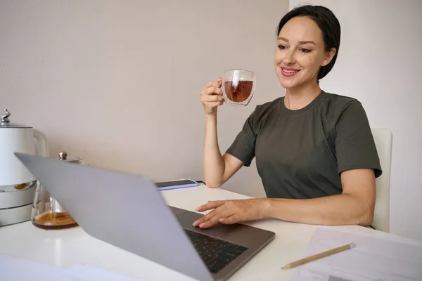 Smiling Woman Sits Table Transparent Cup Tea Looks Laptop — Photo