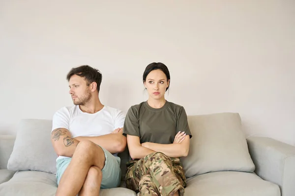 Conflicting Couple Sitting Couch Closed Poses Woman Camouflage Clothes Man — Stockfoto