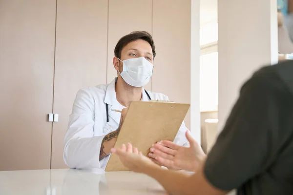 Doctor White Coat Protective Mask Listens Attentively Records Patient Complaints — Stockfoto