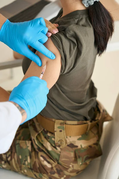 Woman soldier in casual military clothes receives an injection of a vaccine in a special medical center