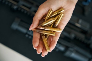 Combat cartridges in a graceful female hand against the background of modern weapons