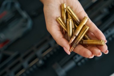 Shiny live ammunition on a delicate female palm against the background of a modern machine gun