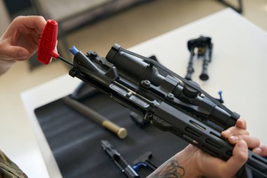 Man cleans a disassembled firearm with a special tool on a napkin, parts of the machine gun are laid out