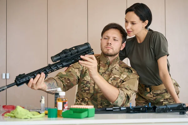 Military man shows a military woman a disassembled machine gun and its parts