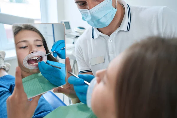 Girl Cheek Retractor Looking Her Teeth Mirror While Doctor Examining — ストック写真