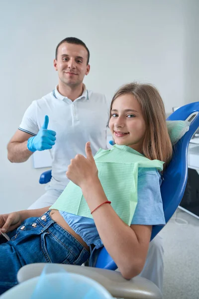 Pediatric Dentist Smiling Pleased Teenage Patient Seated Chair Making Thumbs — Stock fotografie