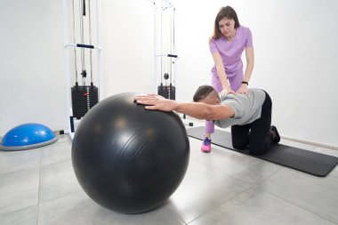 Male patient using physical therapy training equipment while having kinesiotherapy workout with woman physiotherapist
