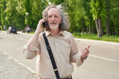 Delighted bearded man keeping smile on his face while talking on telephone