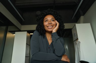 Smiling curly multiracial female in gray blouse in modern office indoor