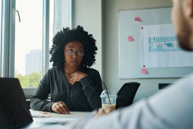Office workers, multiracial woman and man with coffee in their hands communicate calmly at the work table indoors
