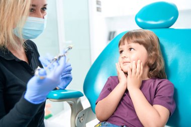 Frightened little girl looking at pediatric dentist with dental syringe in hands