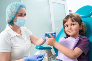 Tranquil young female patient receiving disposable cup with mouthrinse from pediatric dentist