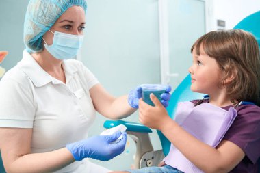 Calm little girl receiving disposable cup with mouthwash from professional dental hygienist